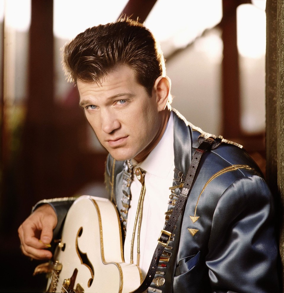 Chris Isaak as a young man, 1990, photo with a white guitar in a blue suit